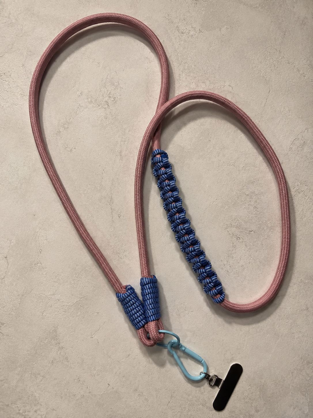Różowo-granatowy phone strap crossbody ułożony na jasnym kamiennym tle