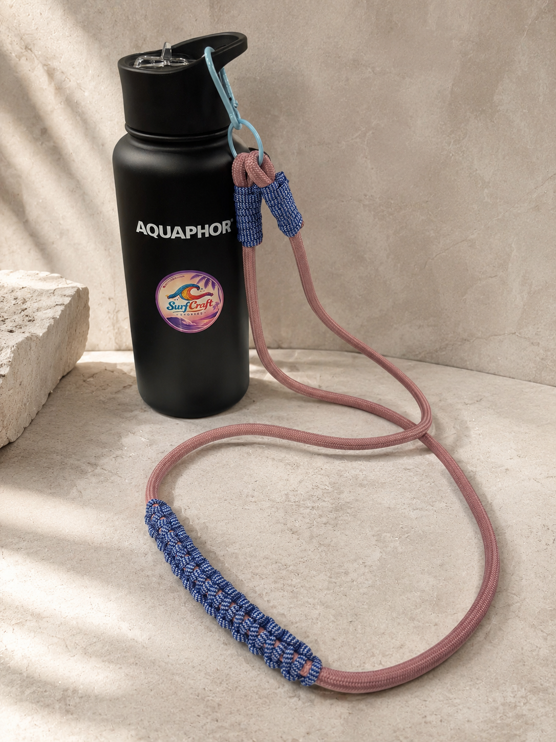 Różowo-granatowy strap crossbody przypięty do czarnej butelki